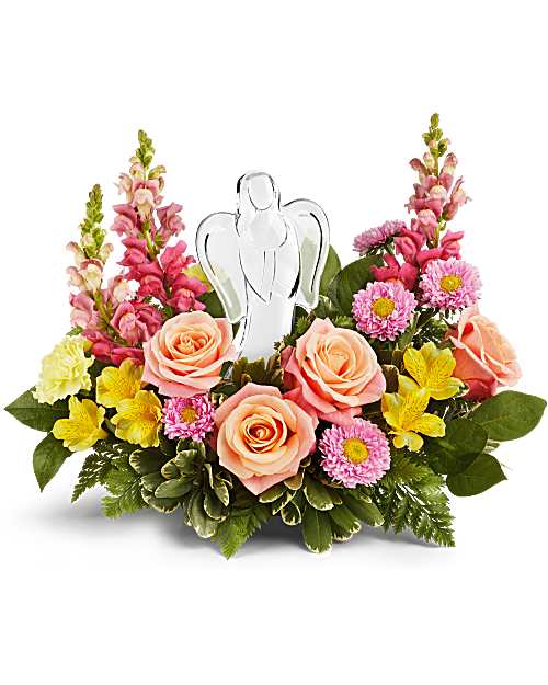 Low arrangement of peach roses and mixed pink and yellow flowers with a glass angel figurine in the center