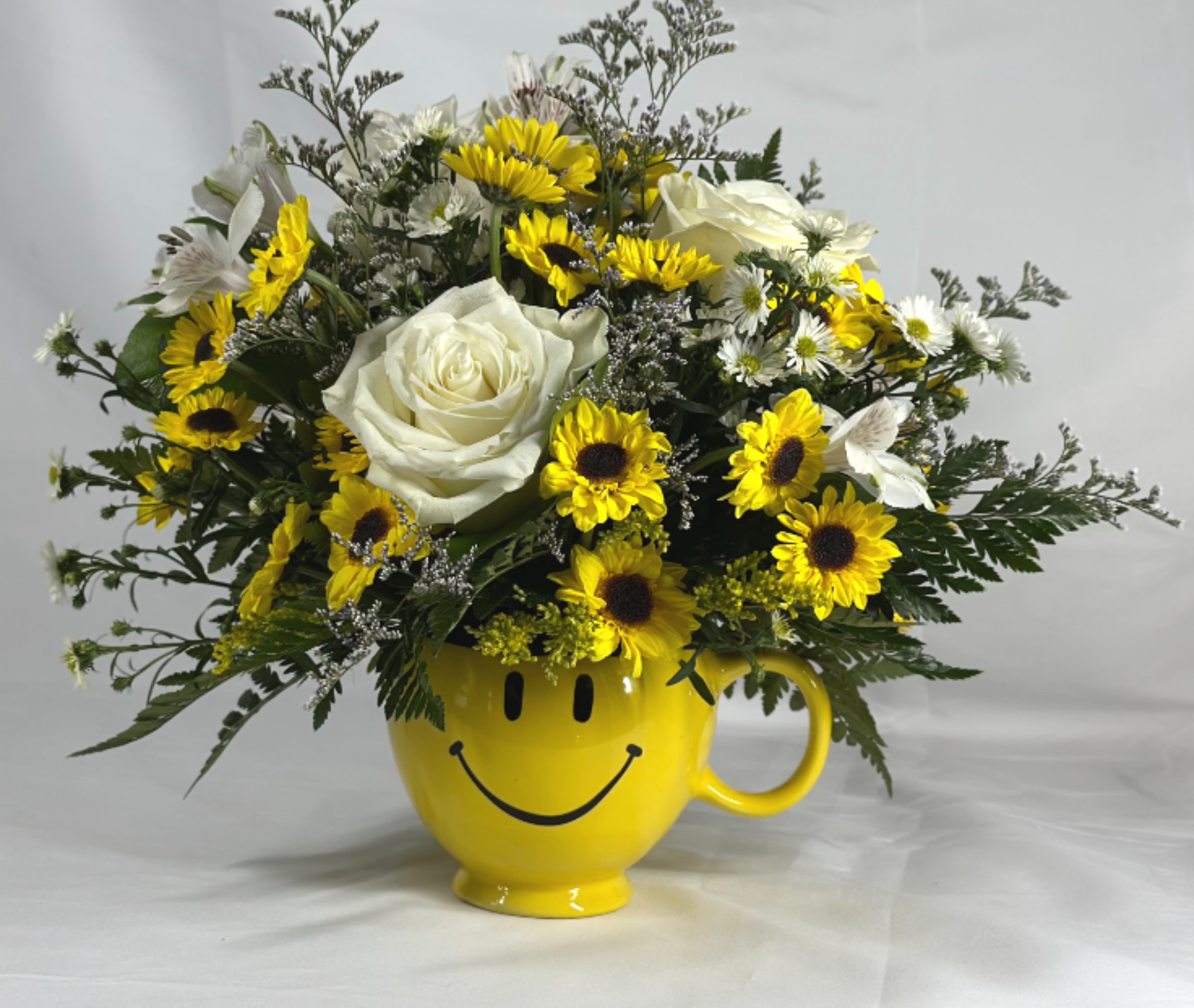 Yellow smiley-face mug holding white roses and yellow daisies
