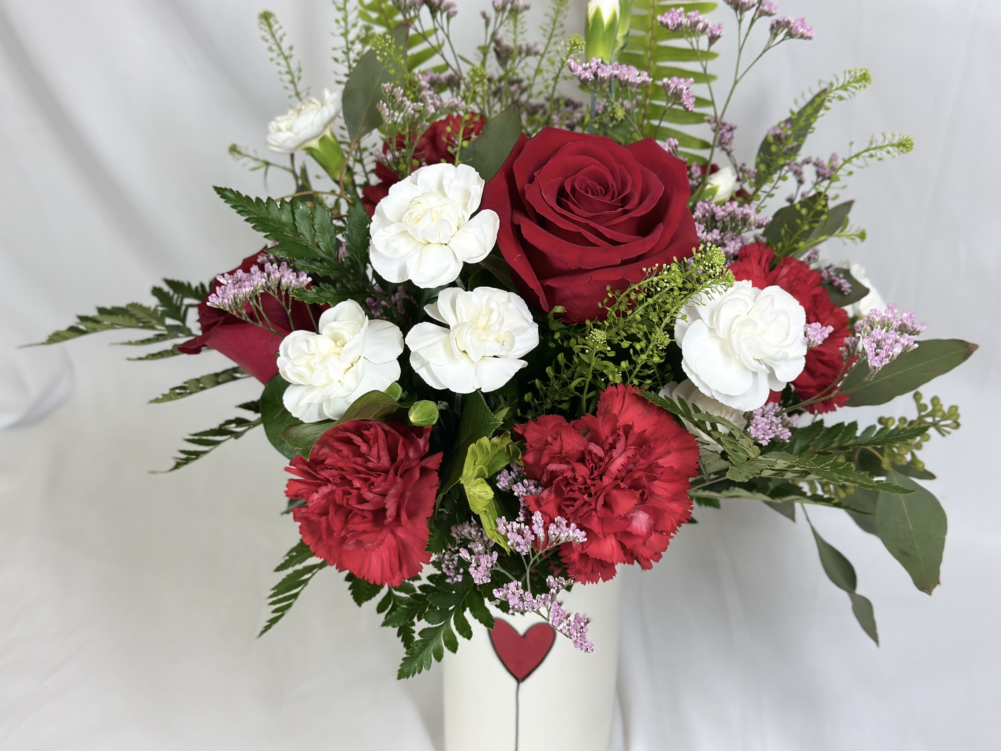 Red roses and white carnations in a white vase.