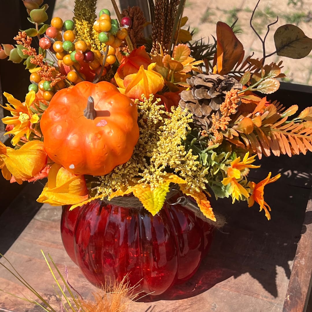 Autumn floral arrangement with a pumpkin and red glass vase