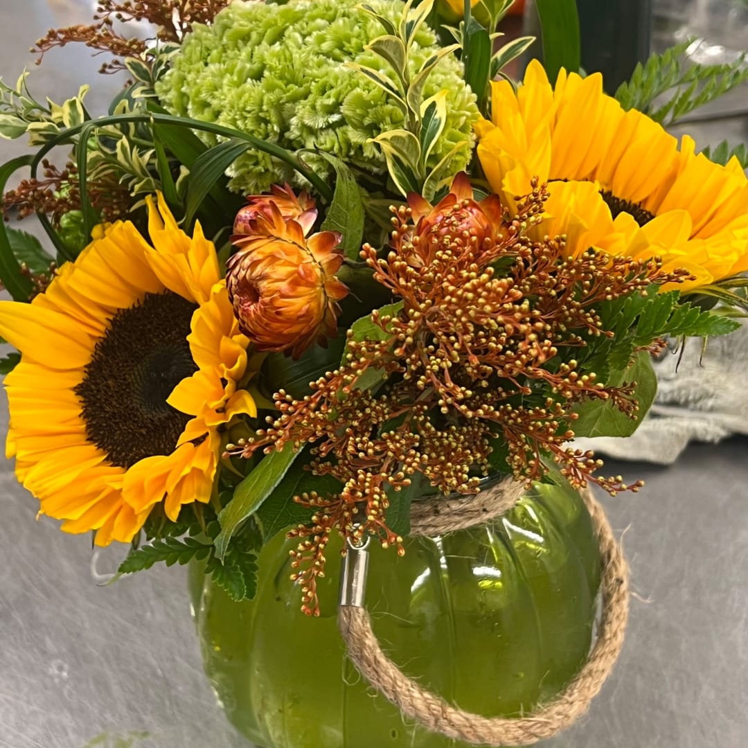Sunflowers and mixed flowers arranged in a green glass pumpkin vase