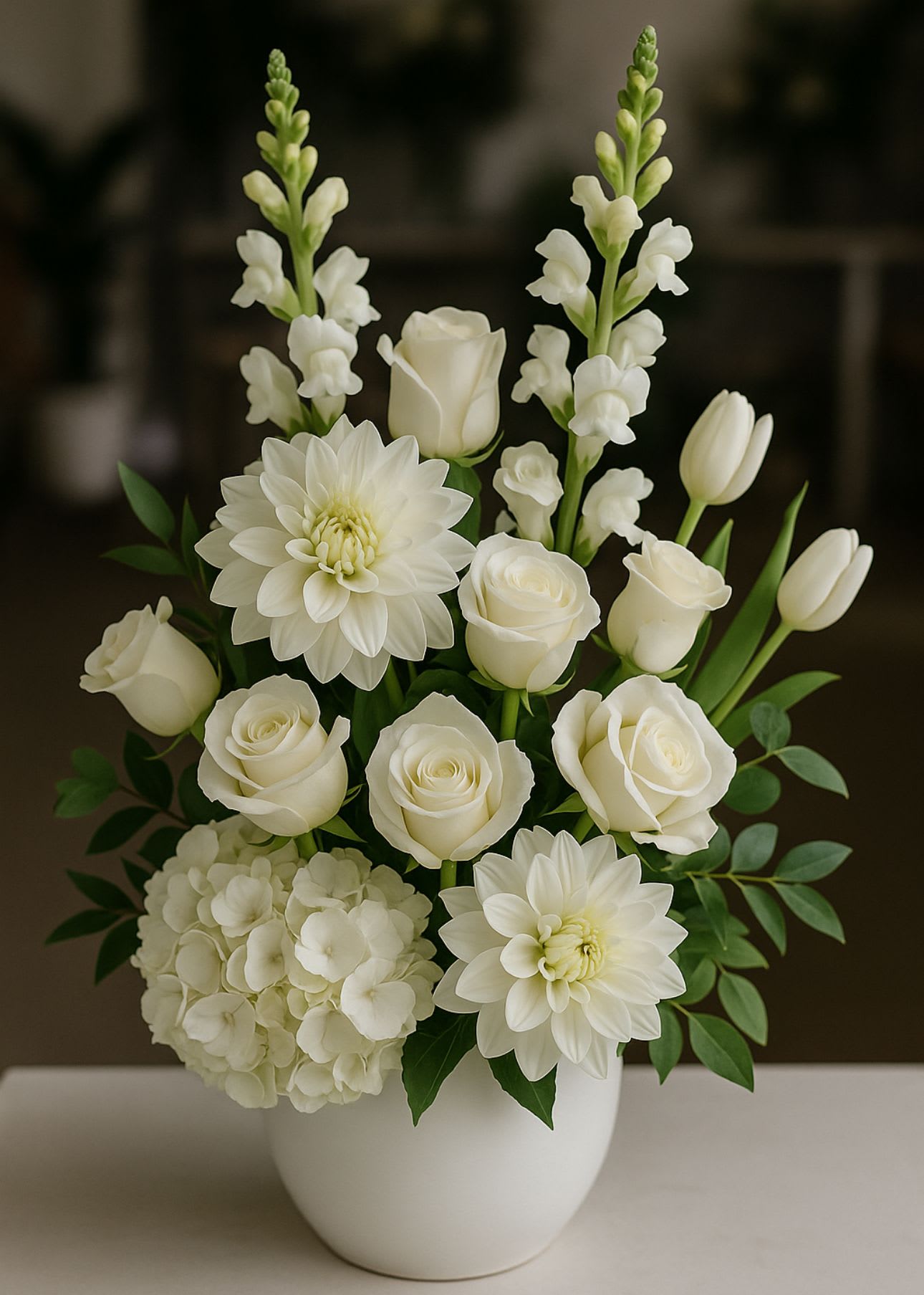 White floral arrangement in a white vase with roses, dahlias, hydrangea, and snapdragons