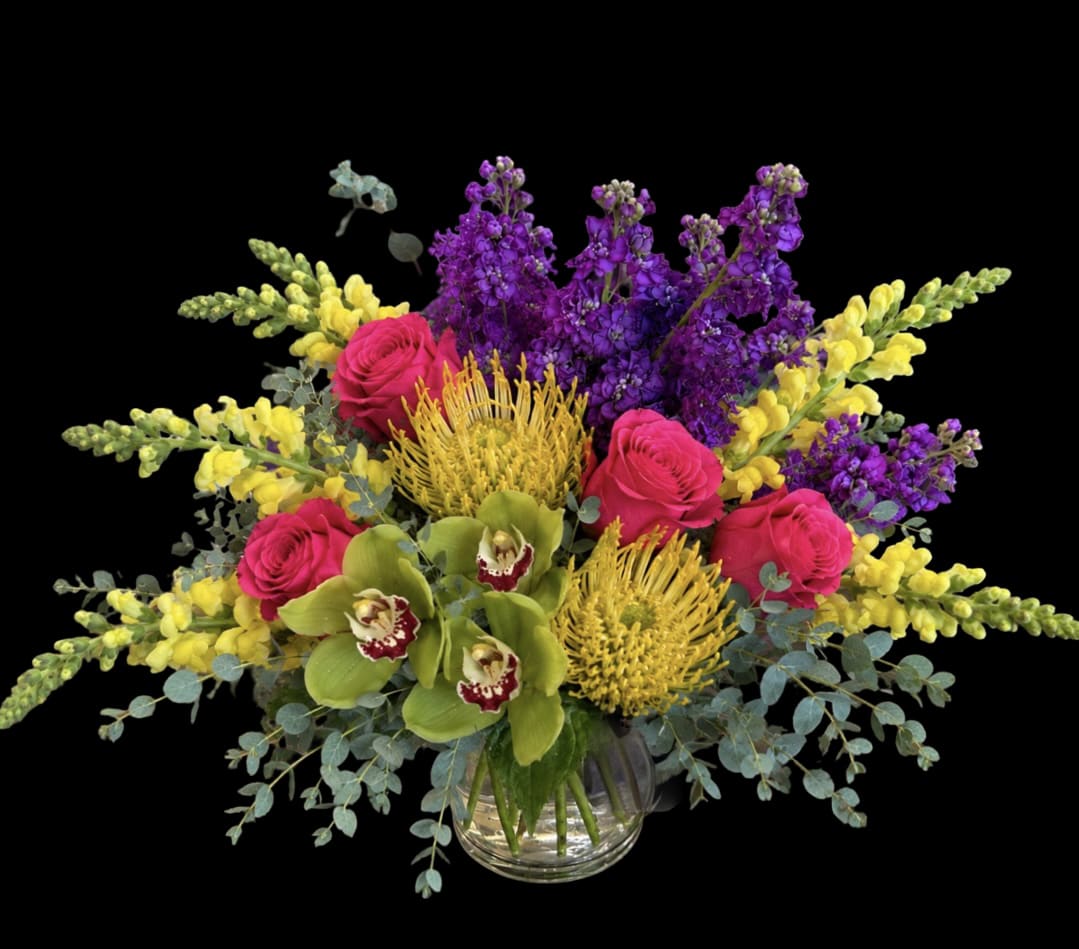     Sunburst Orchid Bouquet  - Hot-pink roses and chartreuse orchids create an immediate burst of color in this flower arrangement, perfect as a New Year celebration bouquet or a bold holiday centerpiece. The Sunburst Orchid Bouquet reads as a lively, tropical-style mixed bouquet that will make the person you're thinking of feel celebrated and uplifted-bright, joyful, and unmistakably festive without feeling seasonal-only.  Tall purple spikes and bright yellow snapdragon-like stems fan outward from two spiky yellow protea heads to give the composition height and drama, while soft blue-green foliage drapes around the base for a finished, garden-fresh look. Mixed roses, orchids, snapdragons and protea are arranged wide and full in a clear glass vase, making this an easy display piece for a mantel, dining table, or entry console.  An excellent choice for holiday gatherings, New Year gifting, or any occasion when you want to brighten someone's day, this arrangement arrives ready to display in the included clear glass vase. To keep blooms looking their best, change the water every couple of days and trim stems slightly-she'll enjoy strong color and texture for several days with basic care.