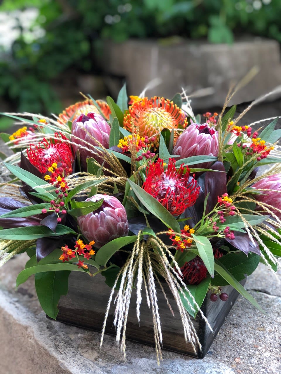Mixed tropical bouquet in a wooden box with pink protea and red-orange blooms