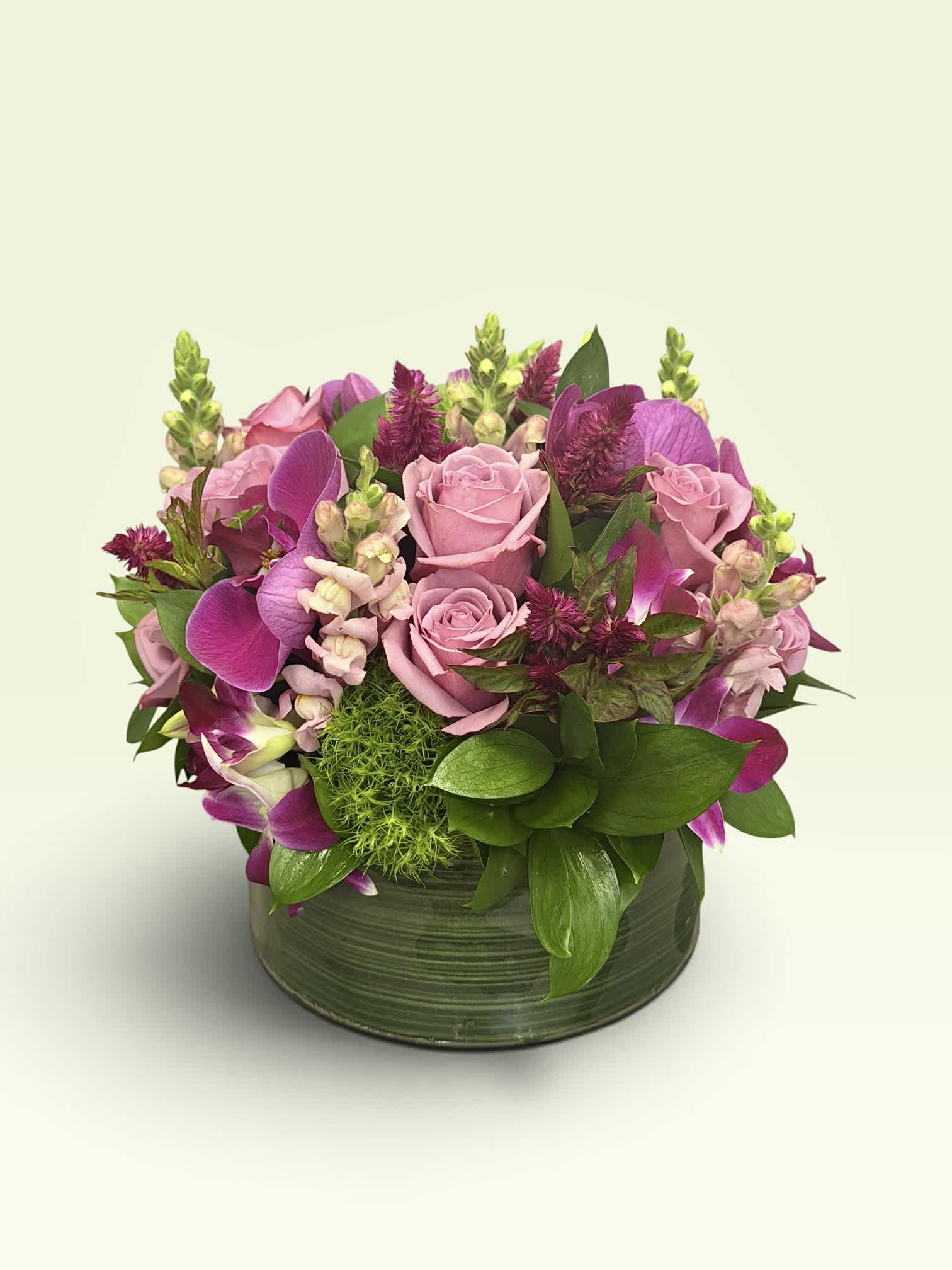 Pink roses and purple orchids arranged in a green round vase