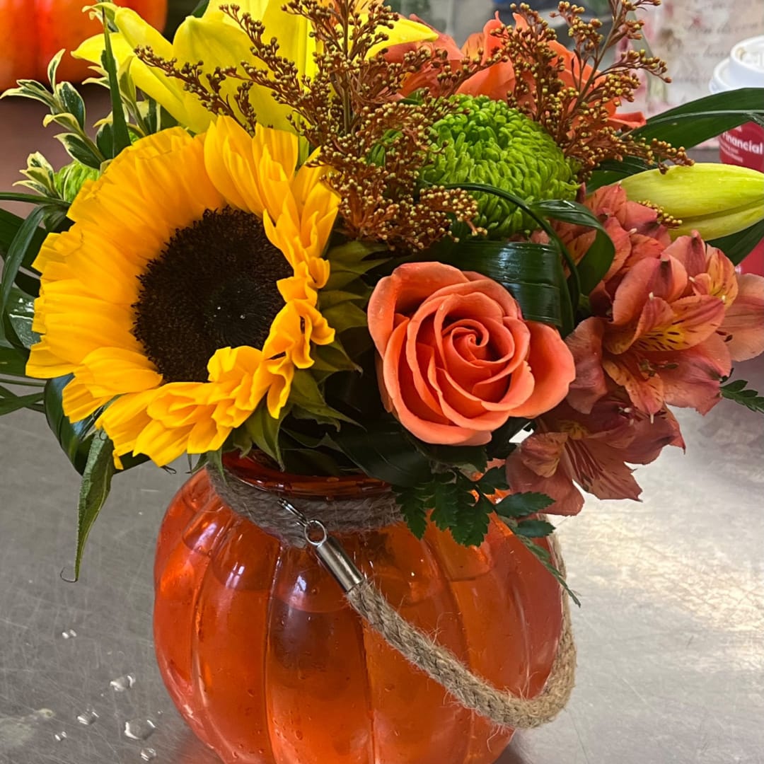 Autumn bouquet with a sunflower, orange rose, and green chrysanthemum in an orange pumpkin vase.
