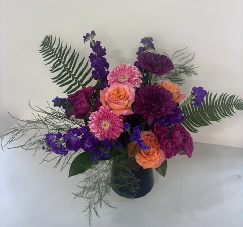 Electric Sunset - Electric Sunset is a striking arrangement bursting with bold color and modern style. Designed in a sleek black vase, it features vibrant hot pink roses, bright pink gerbera daisies, and rich purple stock. This eye-catching design captures the energy of a colorful sunset, making it the perfect statement piece for celebrations, birthdays, or anyone who loves vivid blooms.