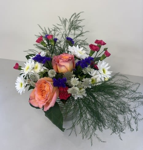 Daisy Dreams Delight - Daisy Dream Delight is a whimsical, garden-inspired arrangement featuring cheerful white daisies, vibrant orange roses, soft pink carnations, and accents of purple statice. This playful blend of color and texture creates a fresh, joyful design that feels like a blooming meadow brought to life, perfect for brightening any occasion.