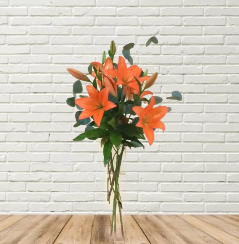 Orange lily bouquet with green foliage in a clear vase