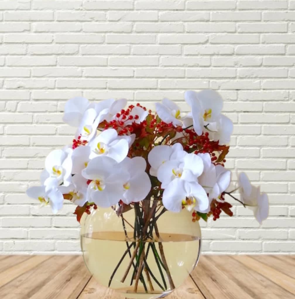 White orchid arrangement in a round glass vase with red berry accents