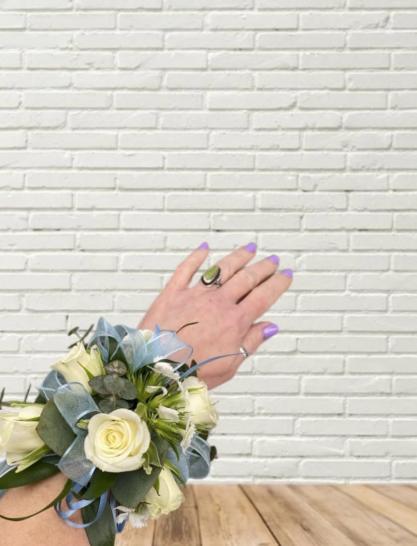 White rose wrist corsage with blue ribbon on a person's wrist