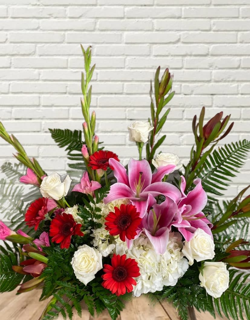 Pink lilies, red gerbera daisies, and white roses in a low arrangement