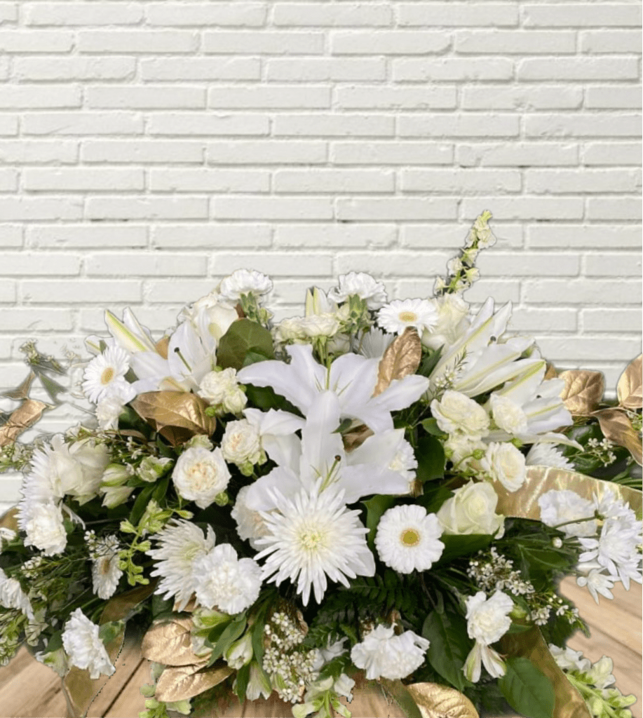 Dipped In Gold Casket Spray - An all white casket spray with dipped in gold greenery and gold bow accents.