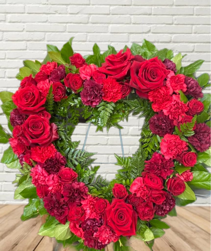Heart-shaped wreath of red roses and carnations with green foliage