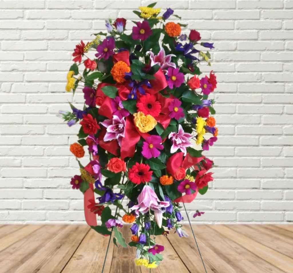 Tall colorful floral standing spray with mixed blooms and a red ribbon