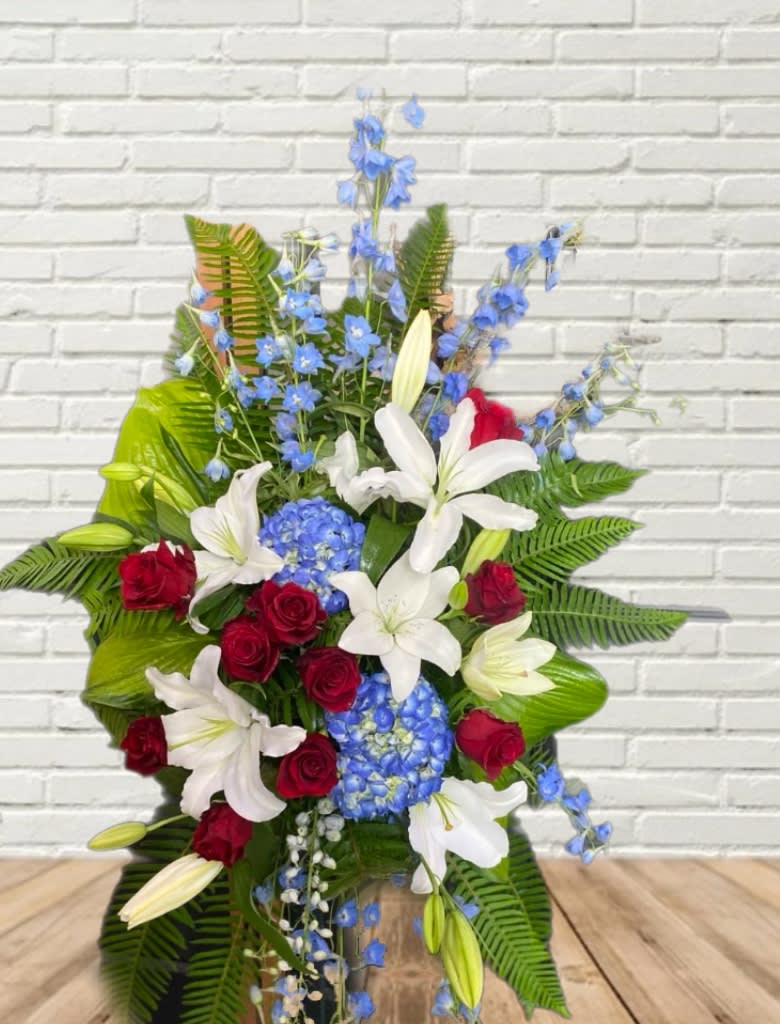 Standing floral spray with red roses, white lilies, and blue flowers