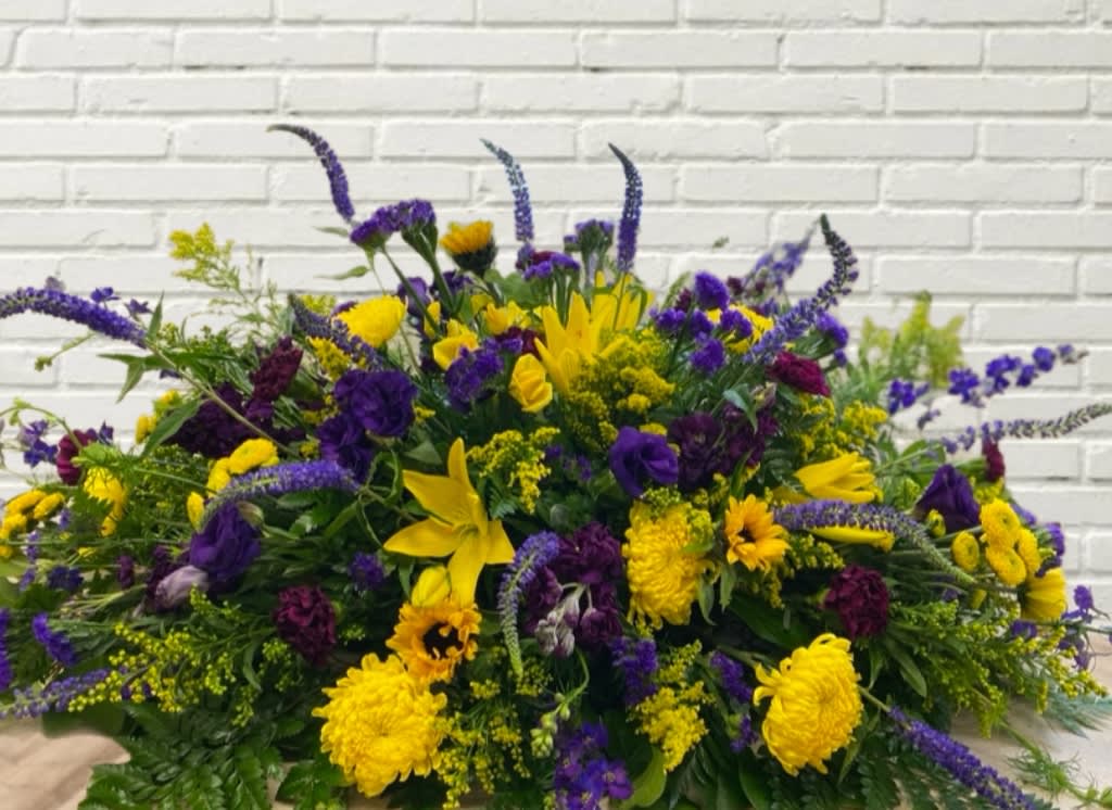 Large yellow and purple floral arrangement against a white brick wall