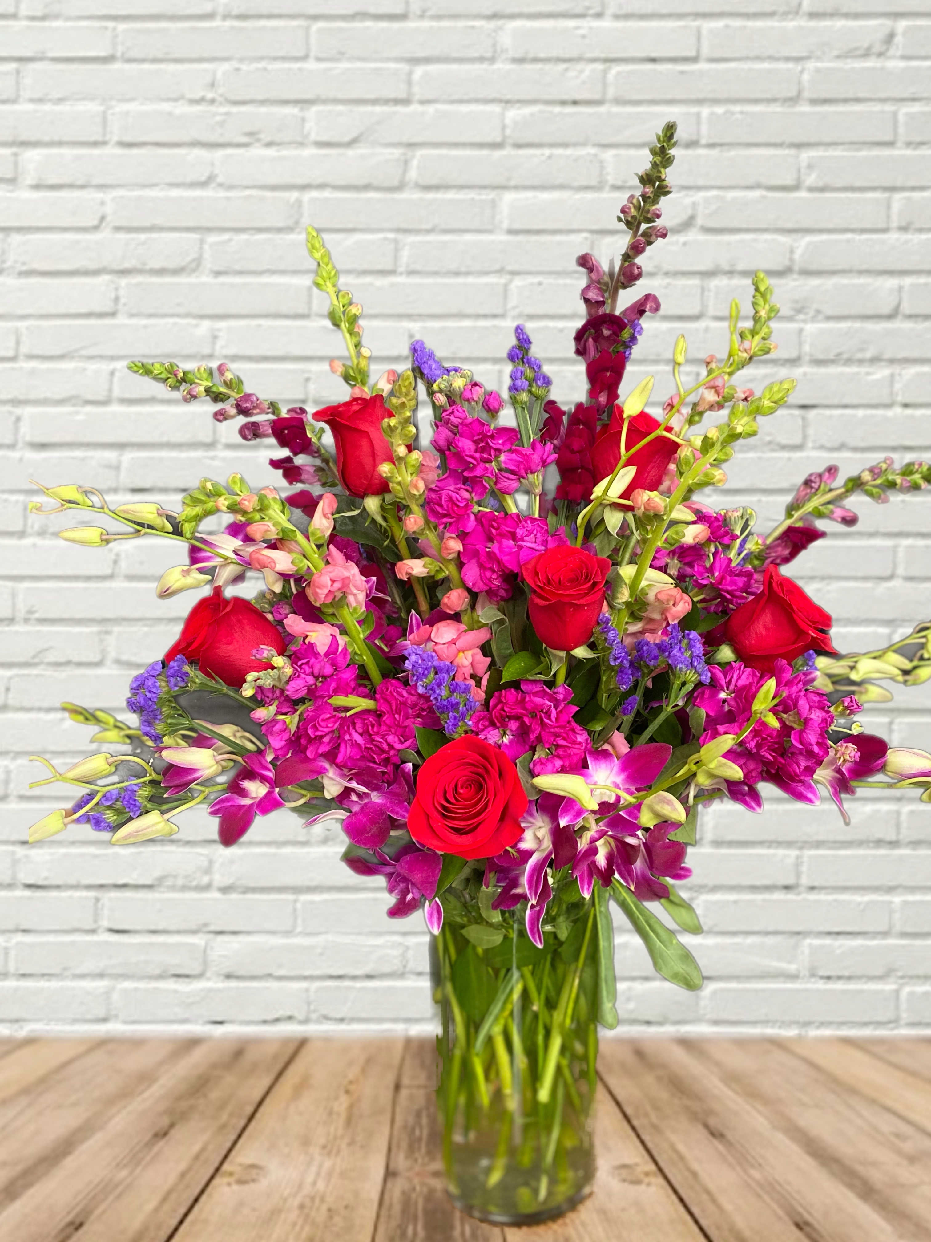 Bouquet of red roses, purple orchids, and pink snapdragons in a glass vase