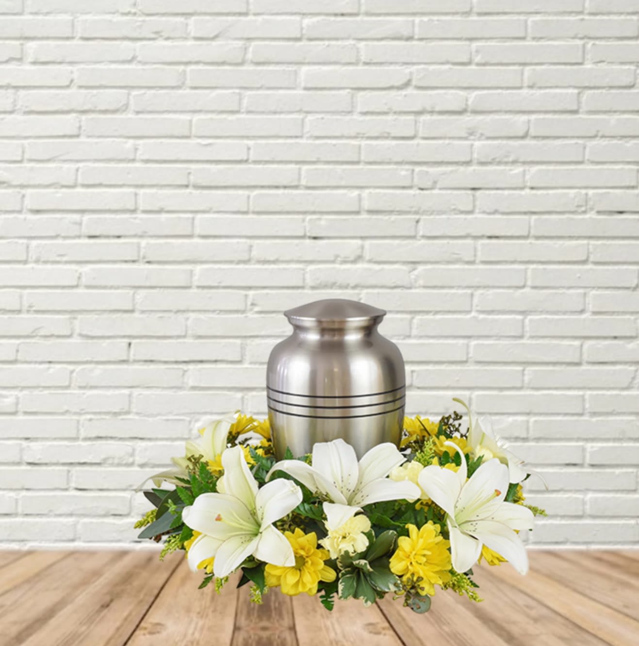 White lilies and yellow flowers arranged around a silver urn