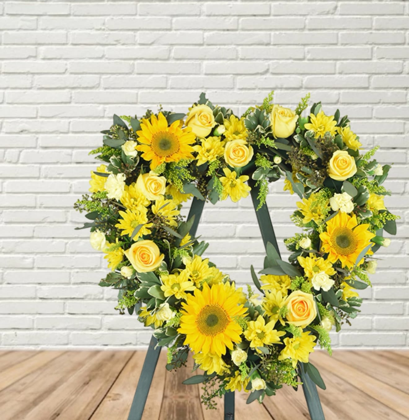 Heart-shaped floral wreath with yellow sunflowers and roses on a stand