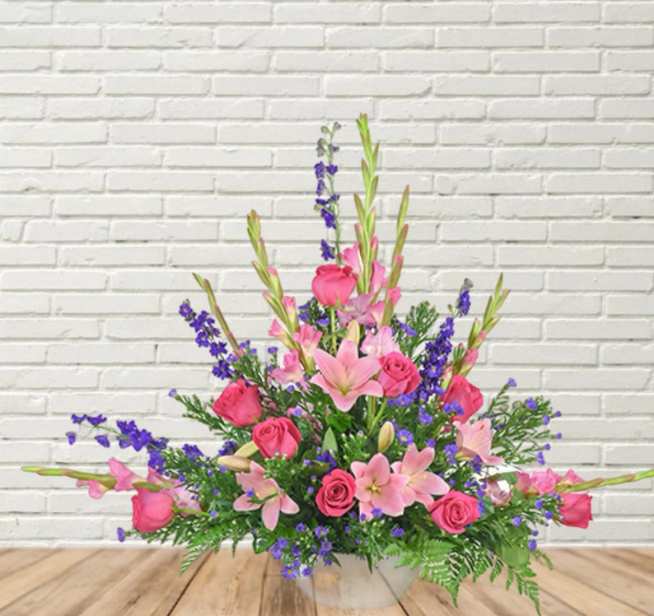 Pink roses and lilies arranged with purple accents in a clear vase.