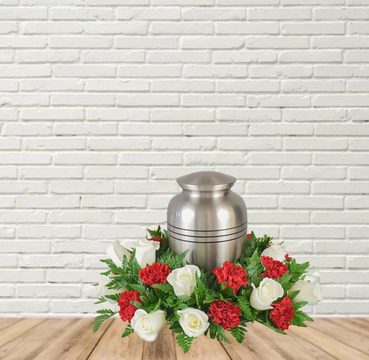 White roses and red carnations arranged around a silver urn.