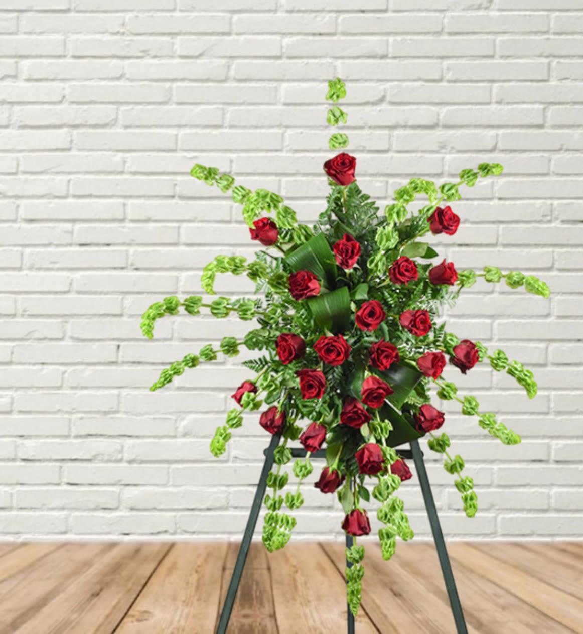 Standing floral spray of red roses with trailing green foliage on an easel