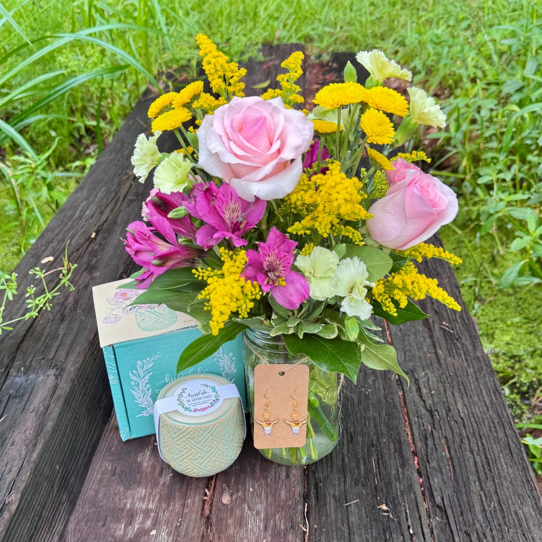 Pink roses and yellow flowers in a glass jar with a candle and earrings nearby.