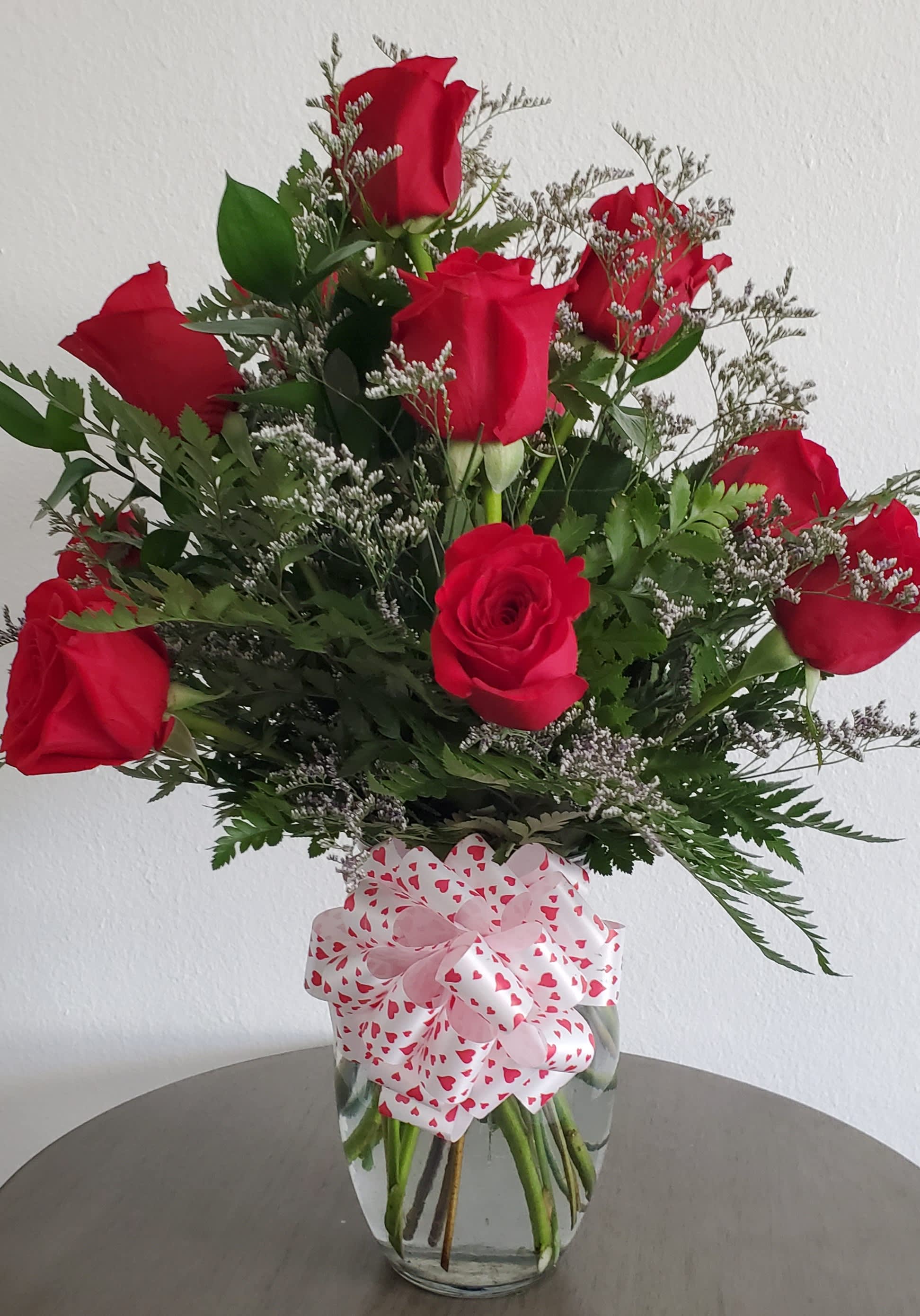 Red roses arranged in a clear glass vase with a heart-patterned bow