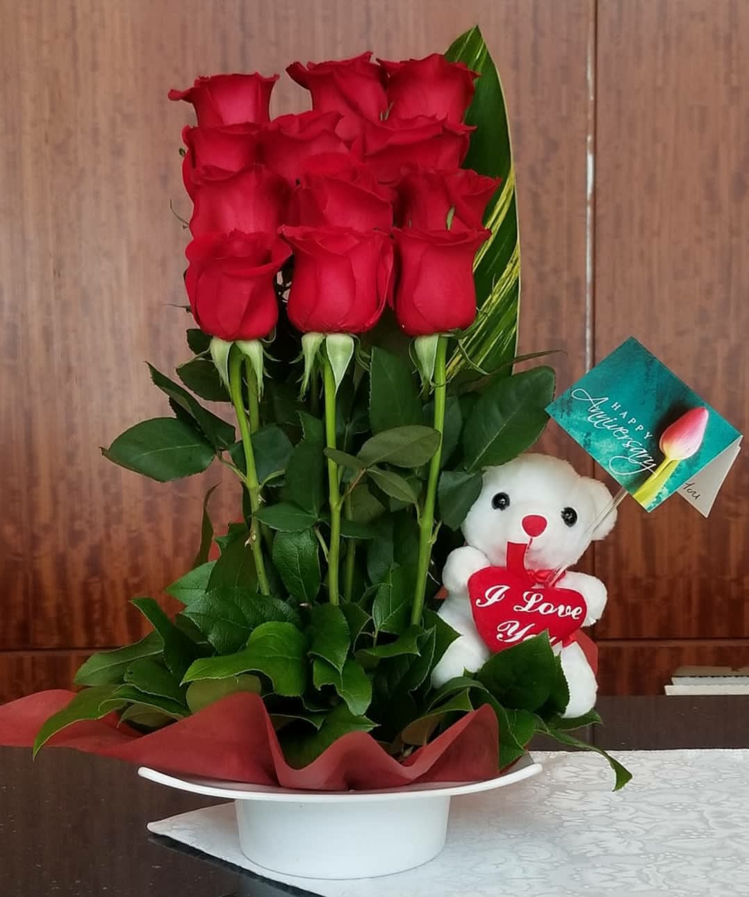 Red roses in a white hatbox with a teddy bear and anniversary tag