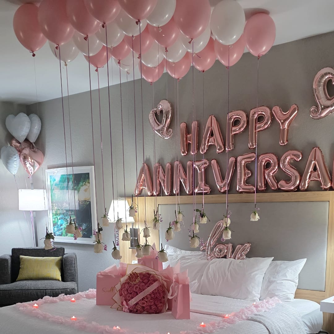 Pink and white balloons over a bed with rose bouquets and anniversary balloons