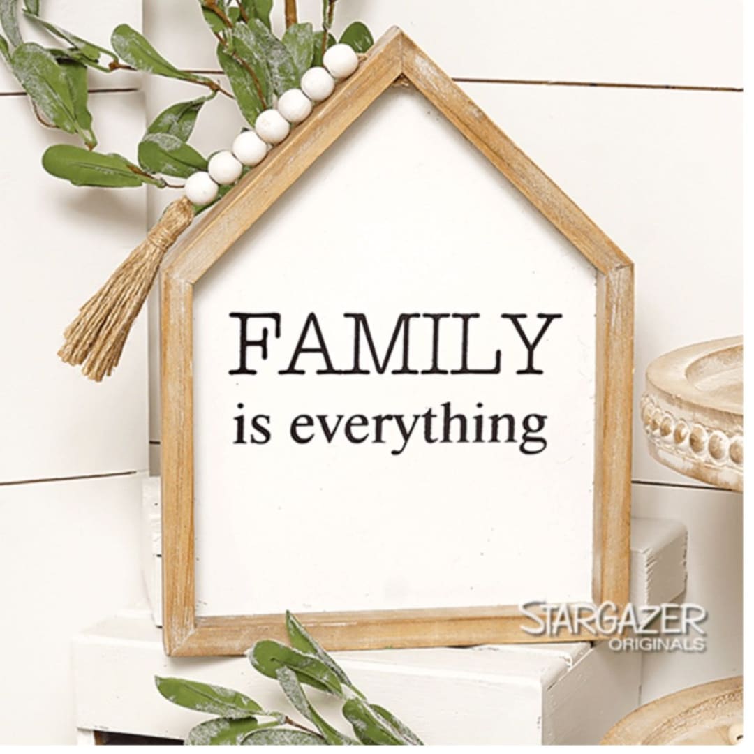 Wooden house-shaped sign reading "FAMILY is everything" with greenery and beads