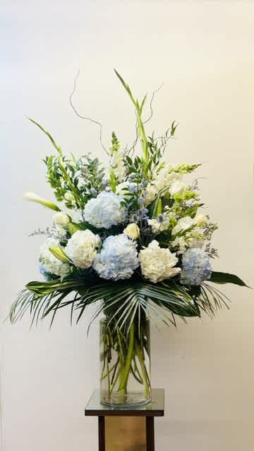 Tall white and pale blue floral arrangement in a glass vase