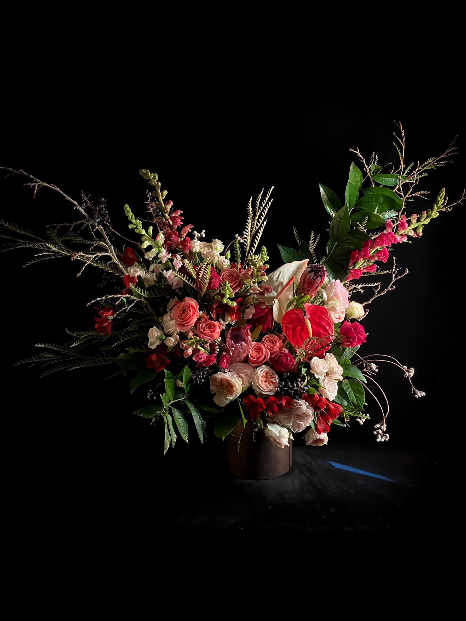 Large floral arrangement with pink and red blooms in a dark vase