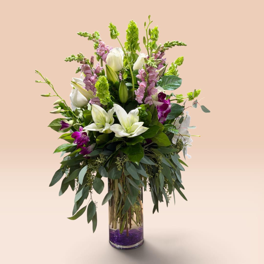 Tall bouquet of white lilies and purple flowers in a glass vase