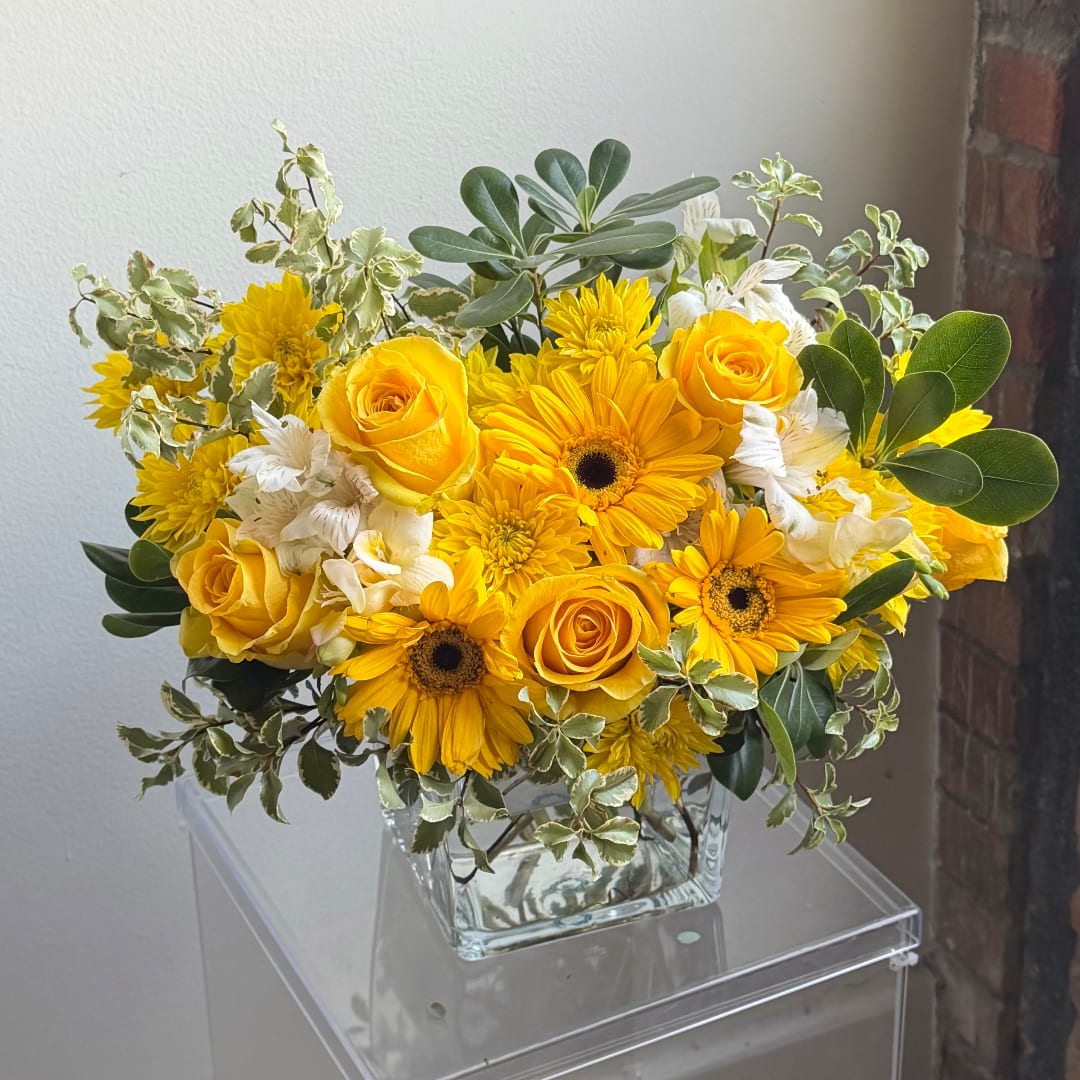 Yellow roses and daisies arranged in a clear glass vase