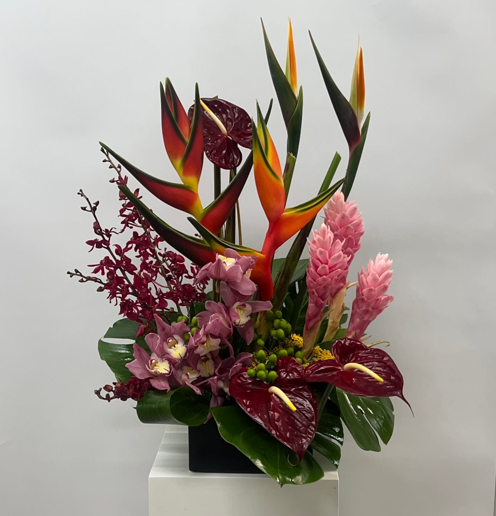 Tropical arrangement with red anthuriums, pink ginger, and orchids in a black container