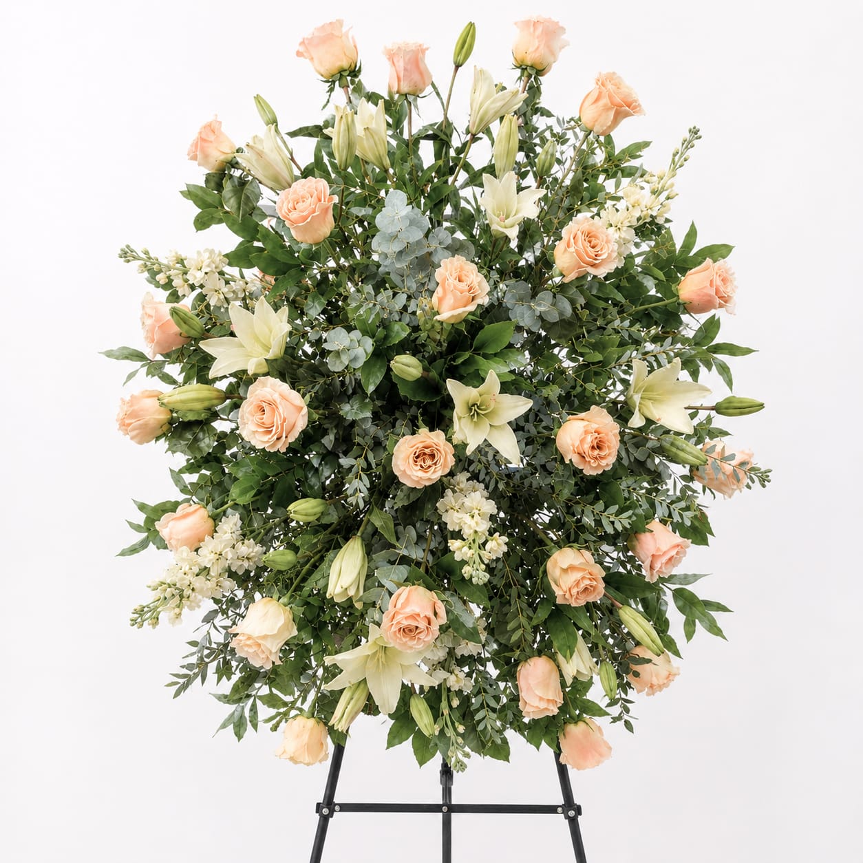 Peach Garden Tribute Standing Spray - Honor a cherished life with the graceful beauty of the Peach Garden Tribute Standing Spray. This elegant sympathy arrangement features a lush blend of soft peach roses, creamy white lilies, delicate stock, and abundant premium greenery, creating a peaceful and uplifting display. Designed on a standing easel, its gentle color palette symbolizes gratitude, remembrance, and everlasting love.  Perfect for funeral services, memorials, or celebration of life ceremonies, this standing spray offers a heartfelt expression of comfort and support to family and friends during difficult times. Handcrafted with fresh, high-quality blooms, it creates a meaningful tribute that reflects warmth, compassion, and dignity.