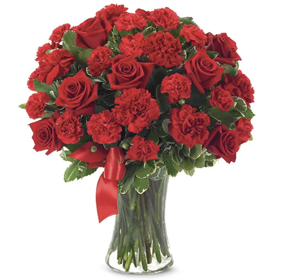 Red roses and carnations in a clear glass vase with a red ribbon