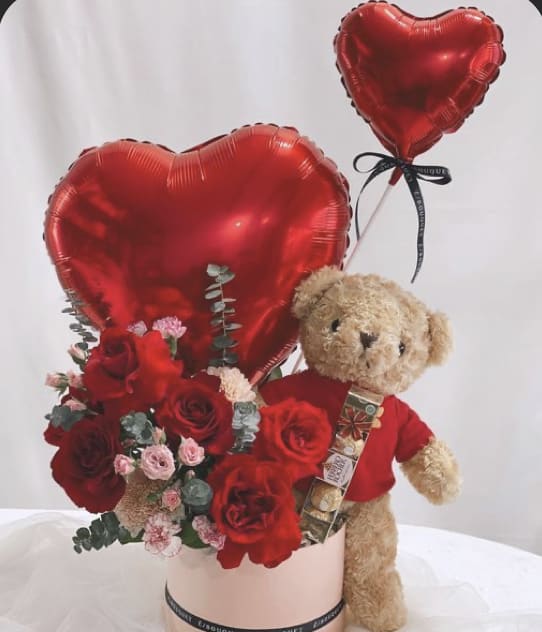 Red heart balloons with roses and a teddy bear in a pink box