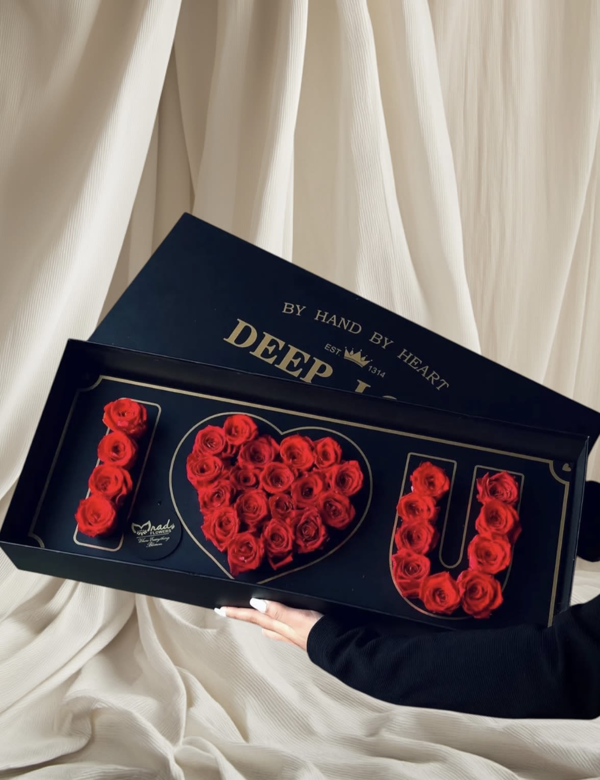 Red roses arranged in a heart and the word LOVE in a black gift box