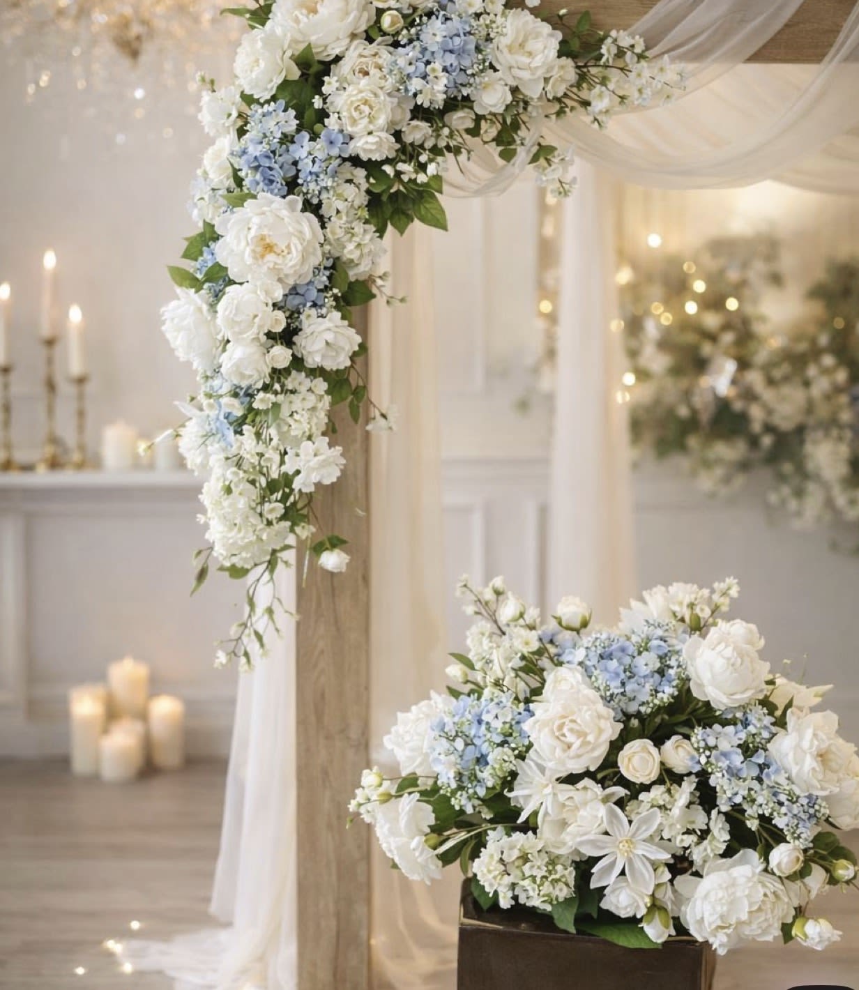 White and pale blue floral wedding arrangements on a draped arch and low pedestal