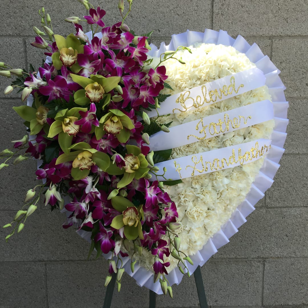 Heart-shaped floral tribute with white flowers and purple orchids on a stand