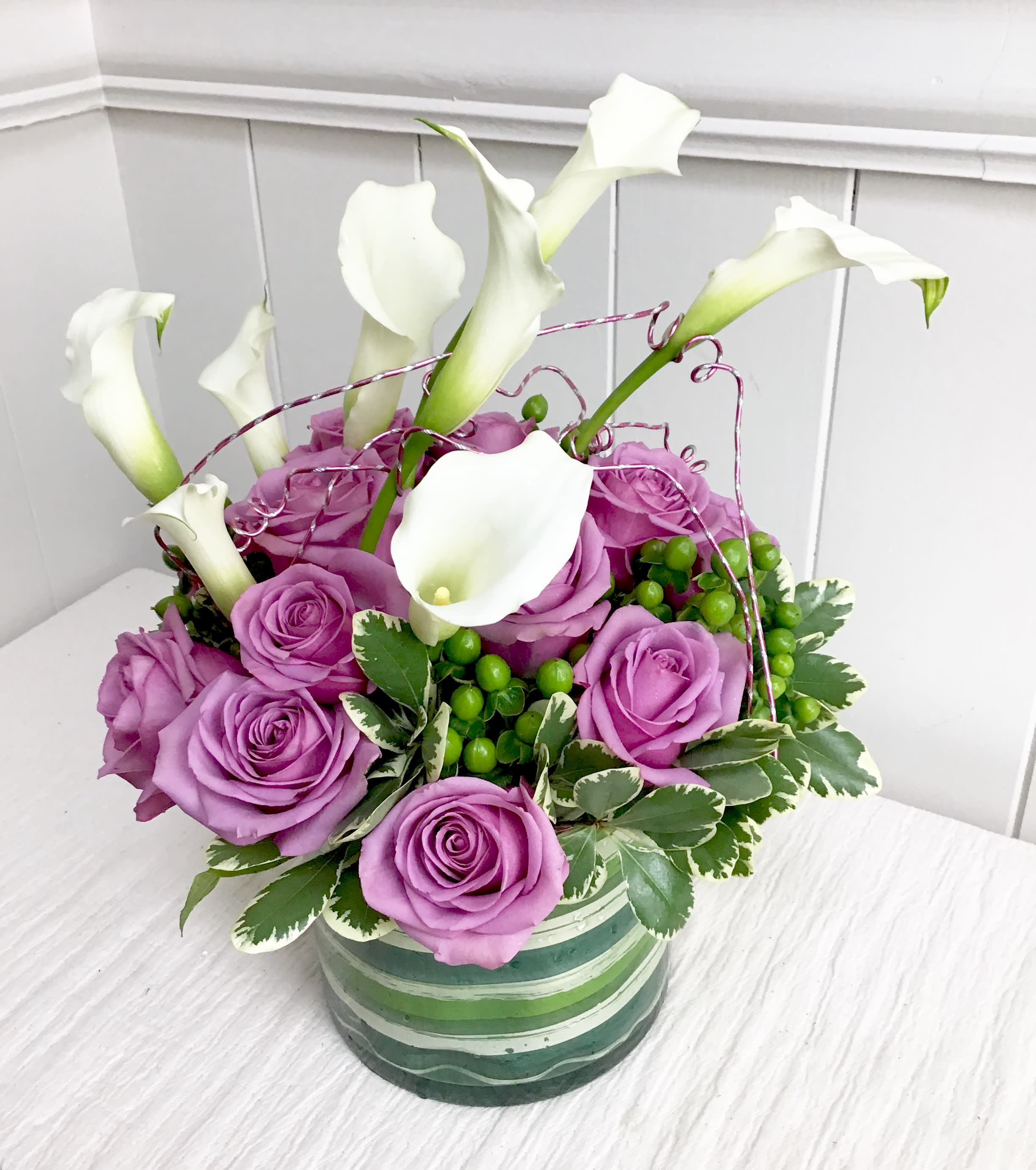 Purple roses and white calla lilies in a striped ceramic vase