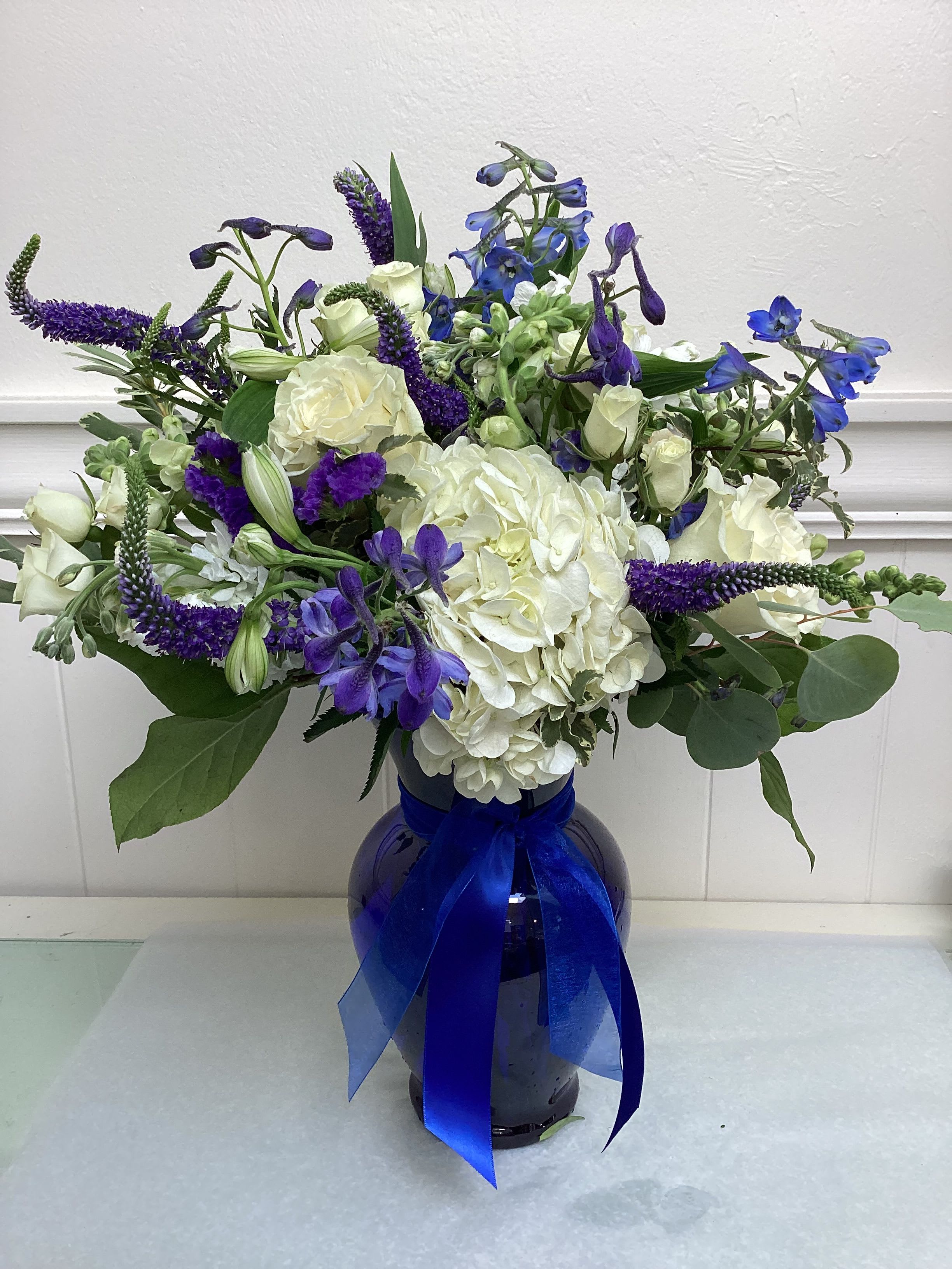 White and blue floral arrangement in a dark vase with a blue ribbon