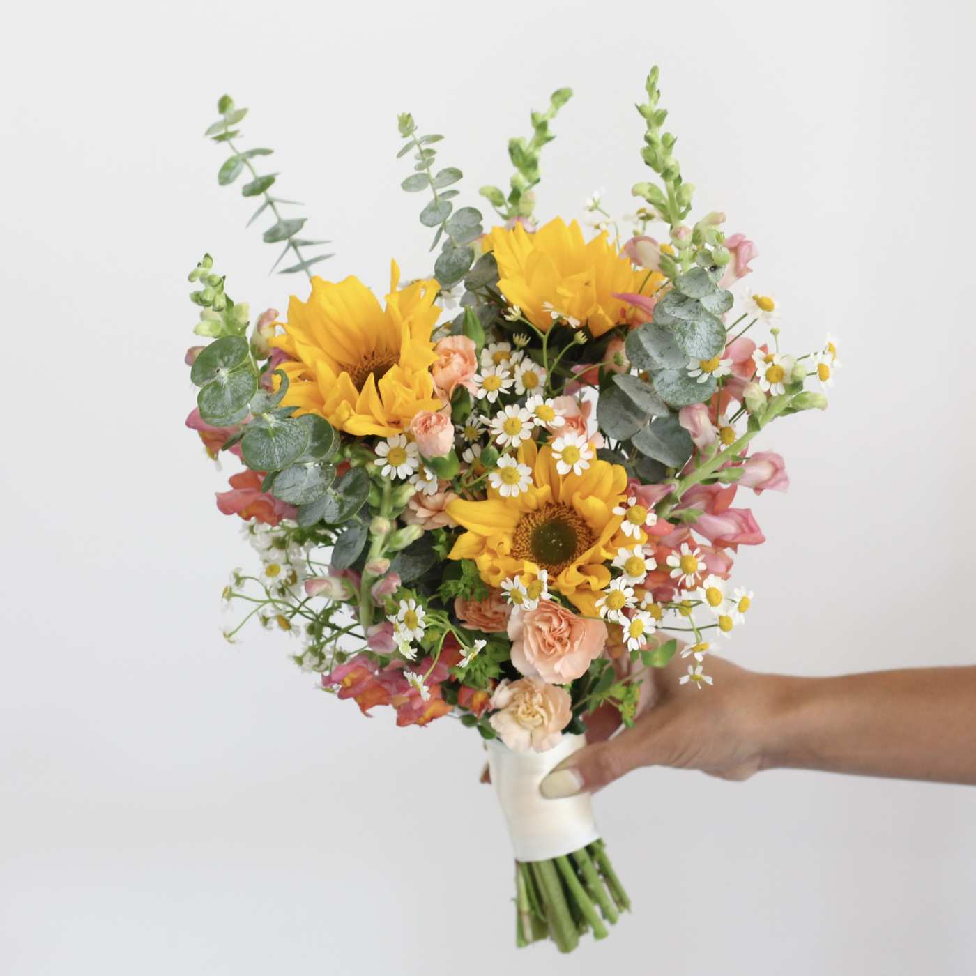 Handheld bouquet with sunflowers, pink blooms, and white daisies