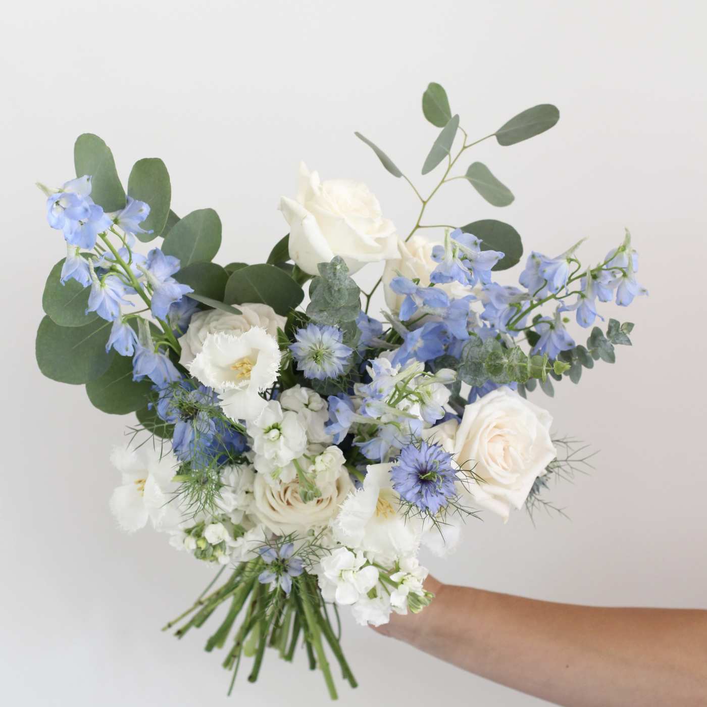 Handheld bouquet of white and pale blue flowers with eucalyptus