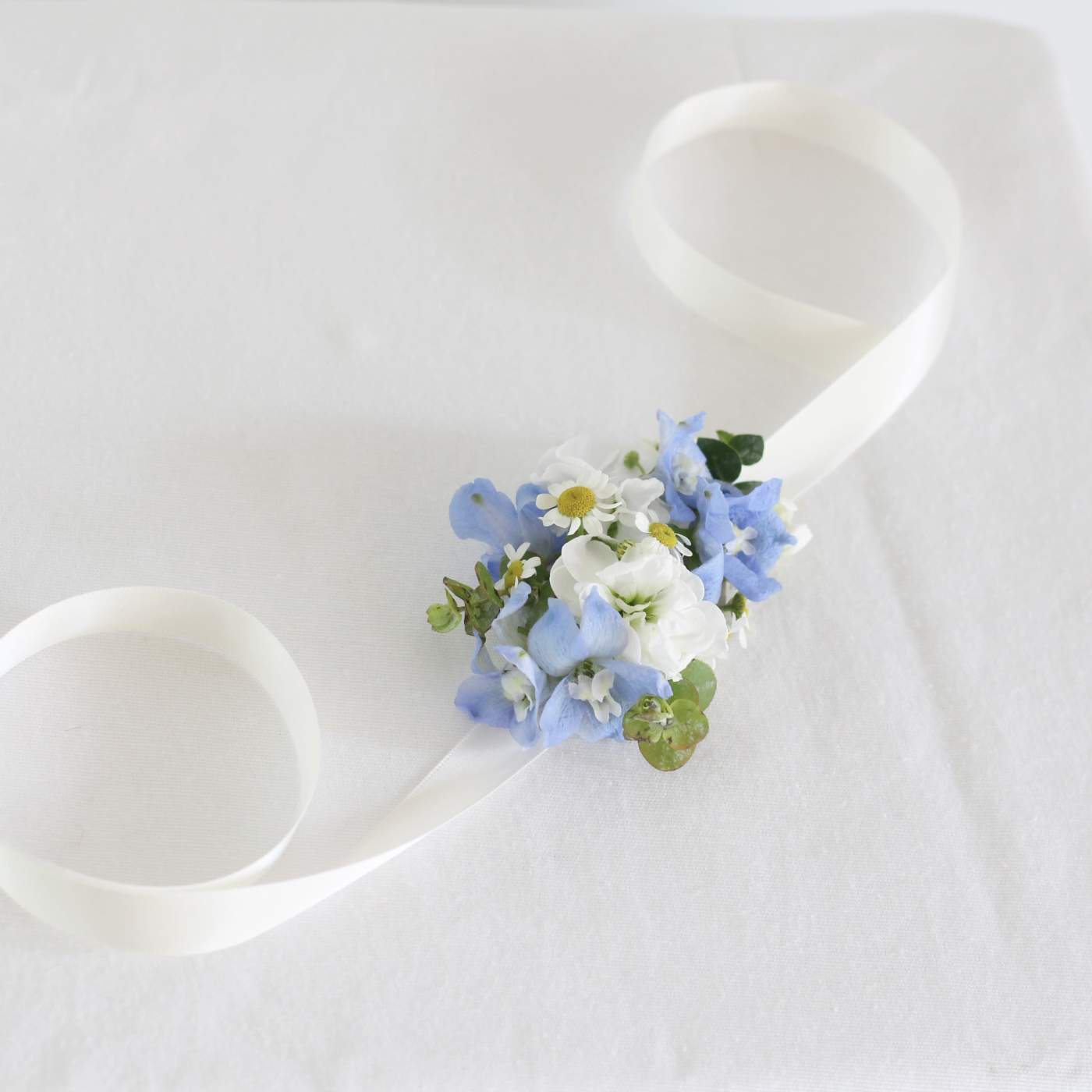 White ribbon wrist corsage with blue and white flowers