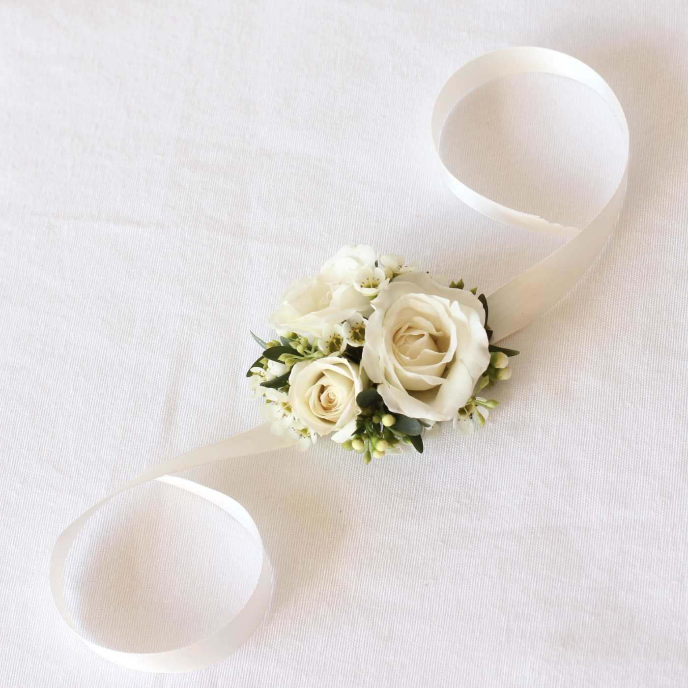 White rose wrist corsage with ribbon ties on a pale fabric background