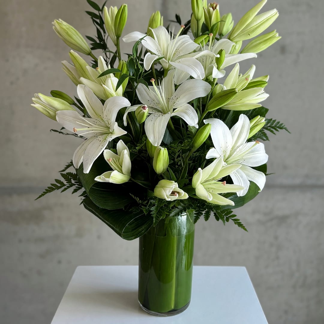 White lilies arranged in a tall green glass vase